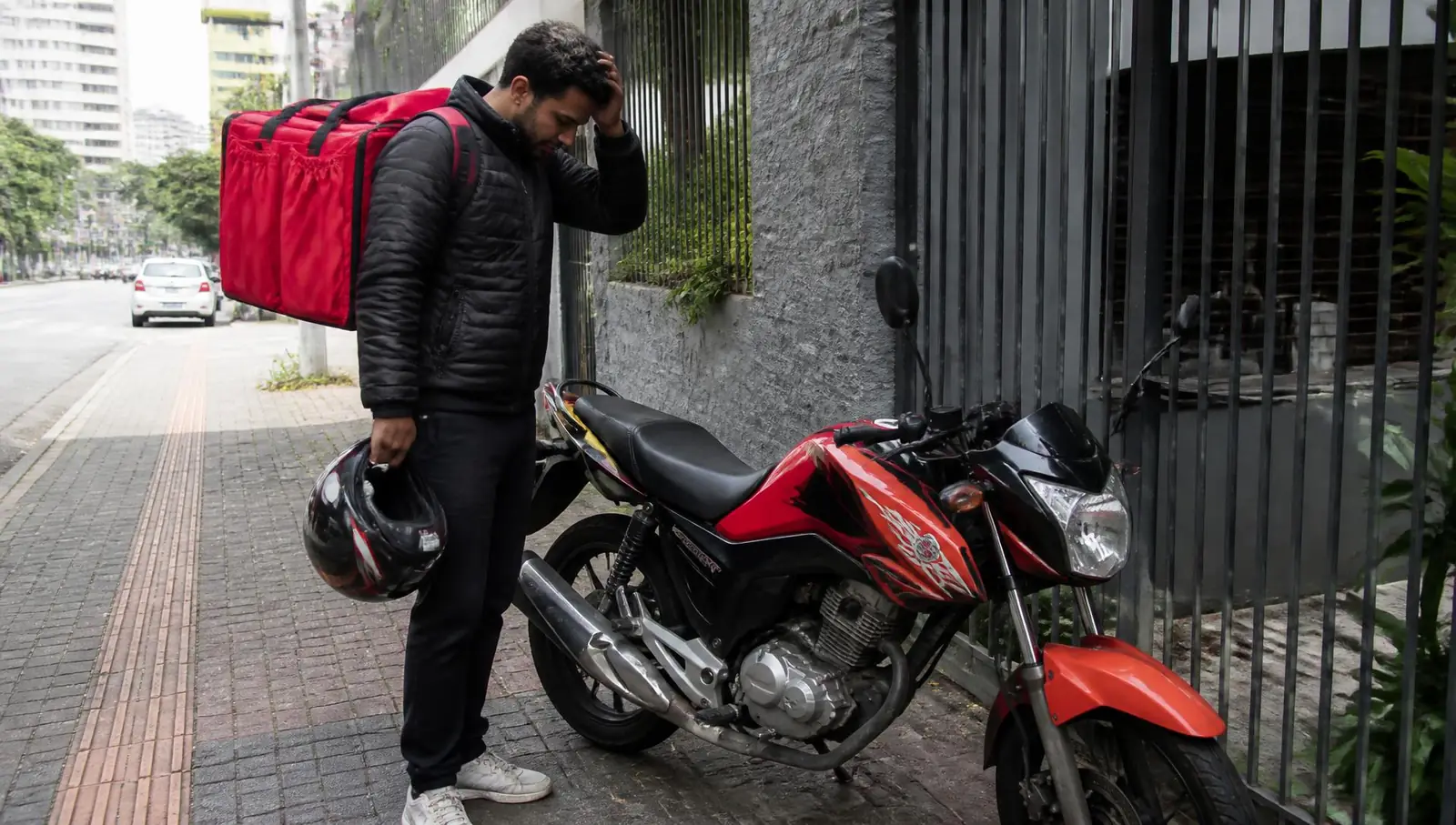 Motociclista entregador ao lado da moto parada esperando socorro de bateria no Rio de Janeiro